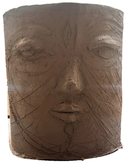 An unfinished cylindrical clay face with closed eyes and visible hand-drawn marks.